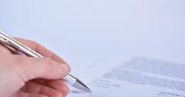 Mãos assinando um documento sobre a mesa, em close