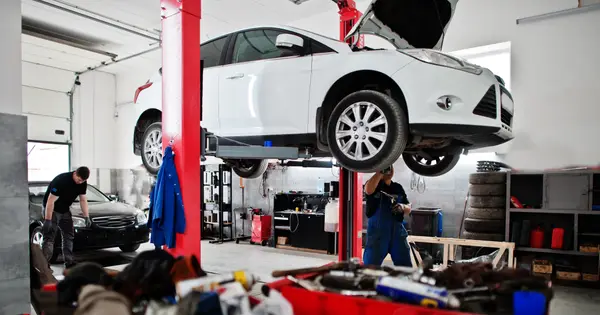 Mecânico de uniforme trabalhando sob o capô de um carro na oficina