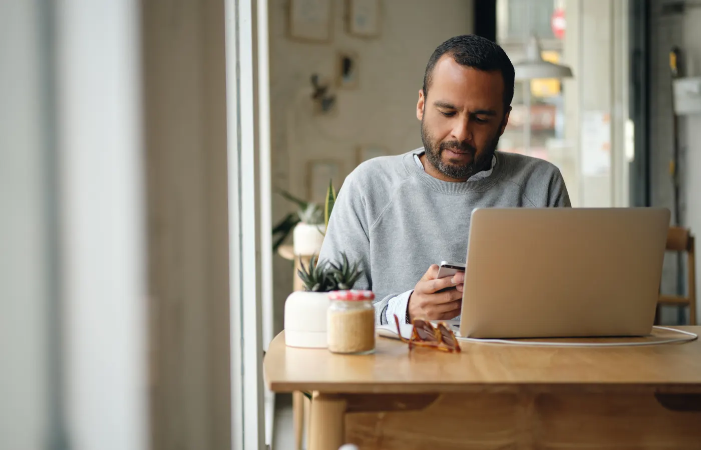 Consumidor pesquisando um serviço no celular enquanto trabalha no notebook